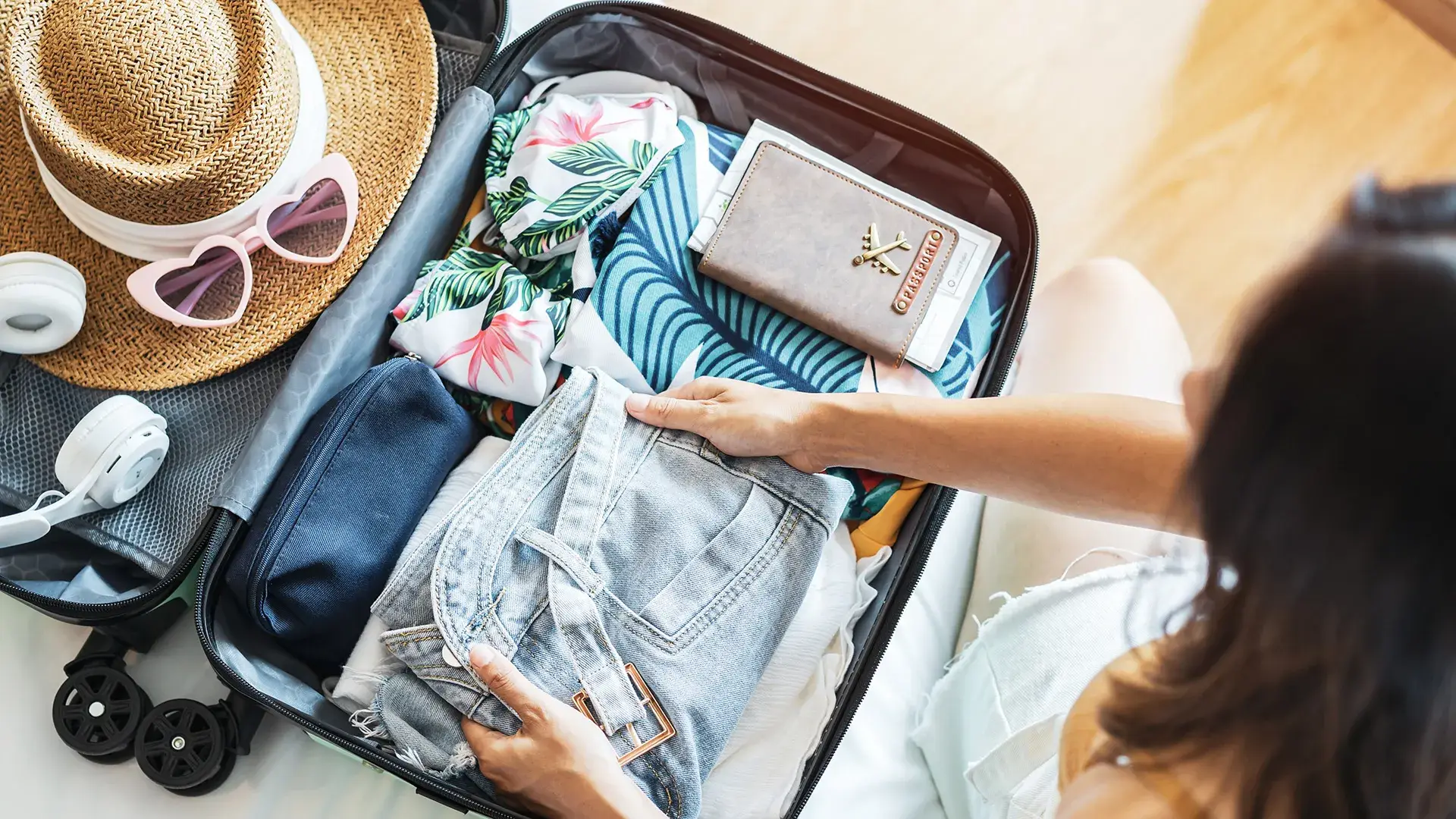 Persona empacando ropa y accesorios de viaje en una maleta abierta.