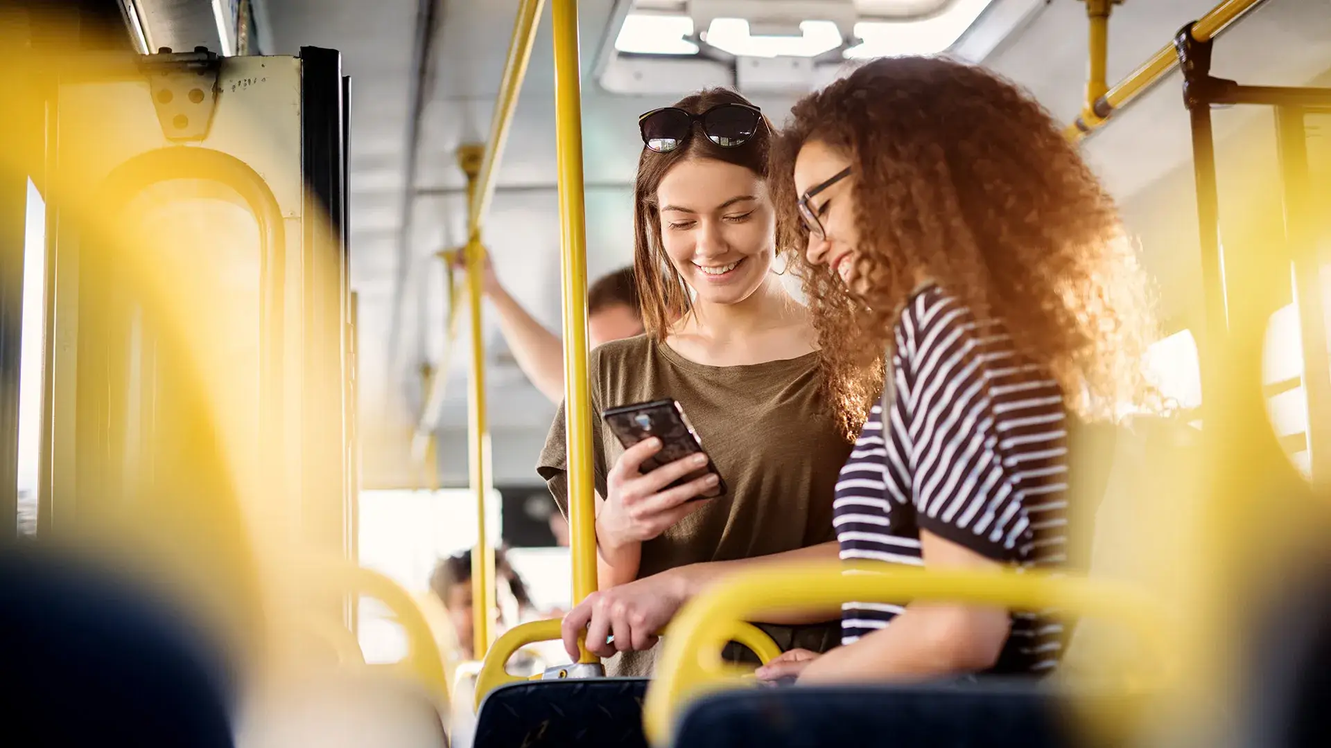 Dos mujeres sonr&iacute;en y miran un tel&eacute;fono en un autob&uacute;s.