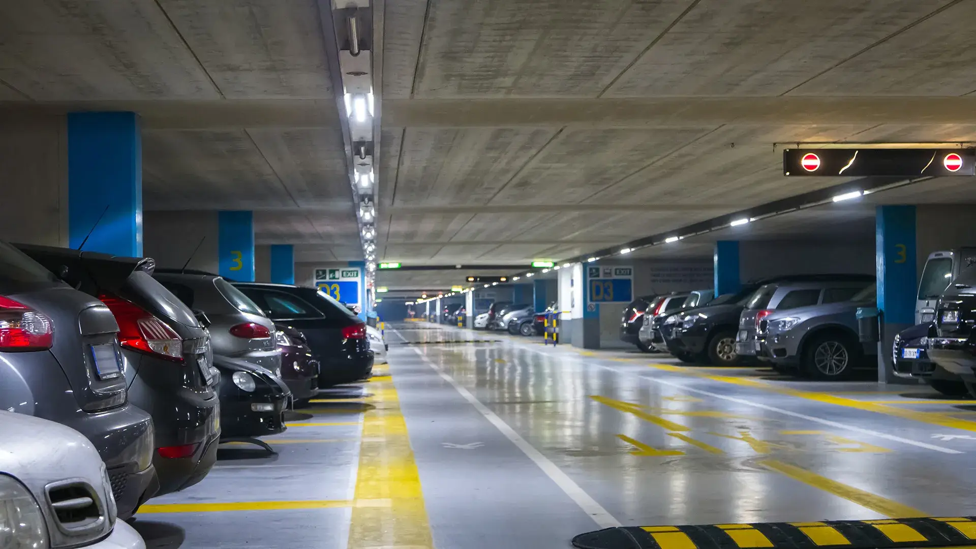 Estacionamiento subterr&aacute;neo iluminado con filas de autos estacionados a los lados.