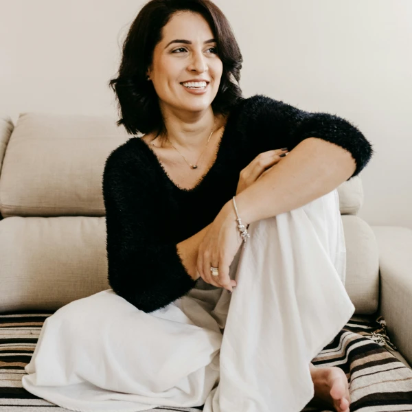 Mujer sentada sonriendo con ropa c&oacute;moda en un sof&aacute; beige.