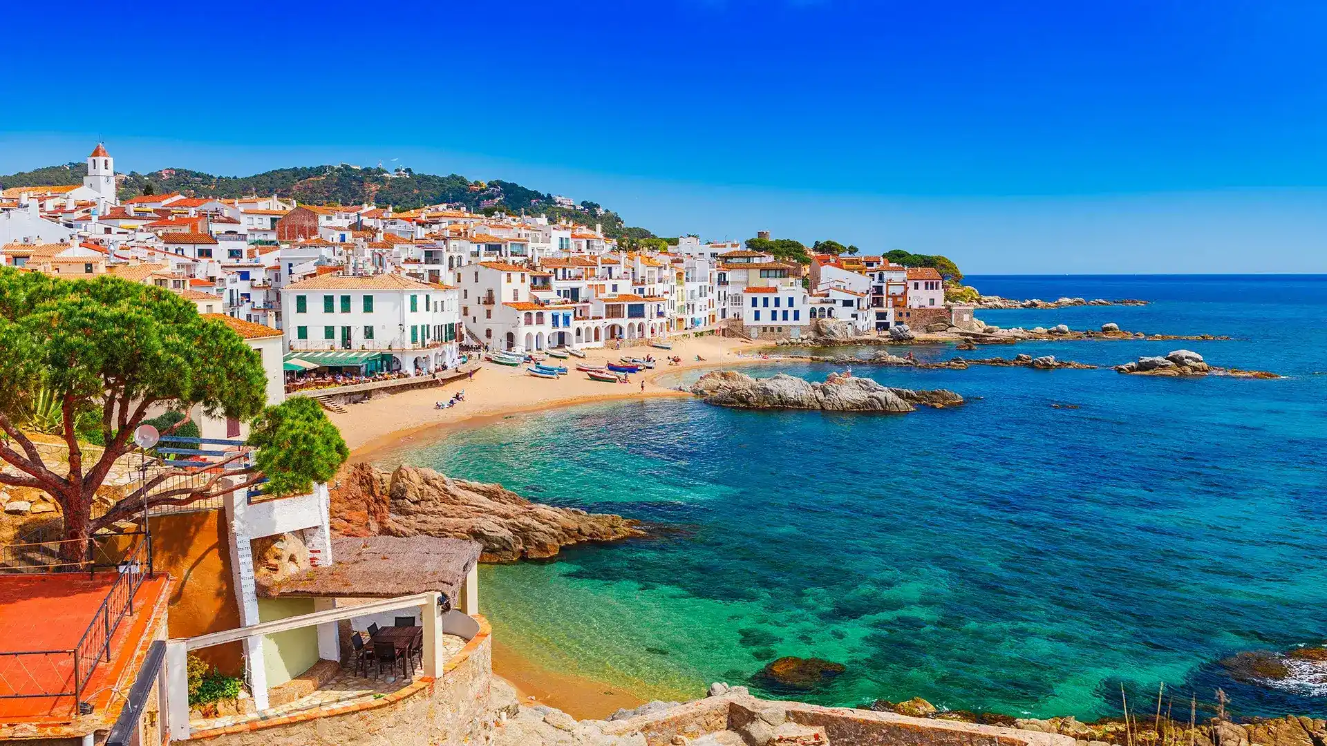 Pueblo costero mediterr&aacute;neo con playa, casas blancas y cielo despejado.