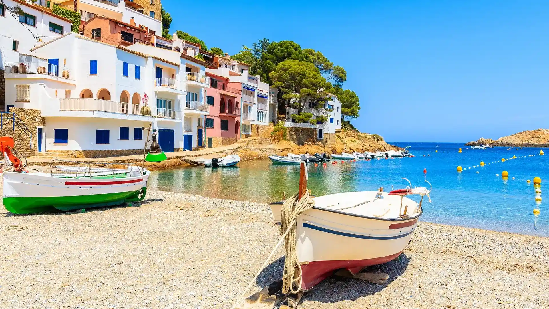 Casas coloridas y barcas en una cala mediterr&aacute;nea con agua cristalina.