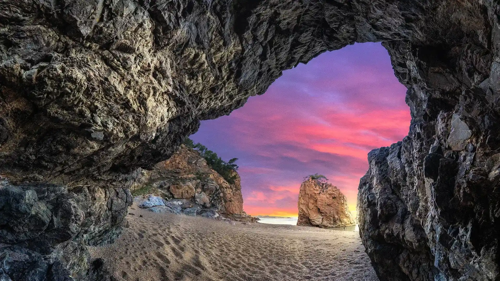 Vista de una playa al atardecer desde el interior de una cueva rocosa.