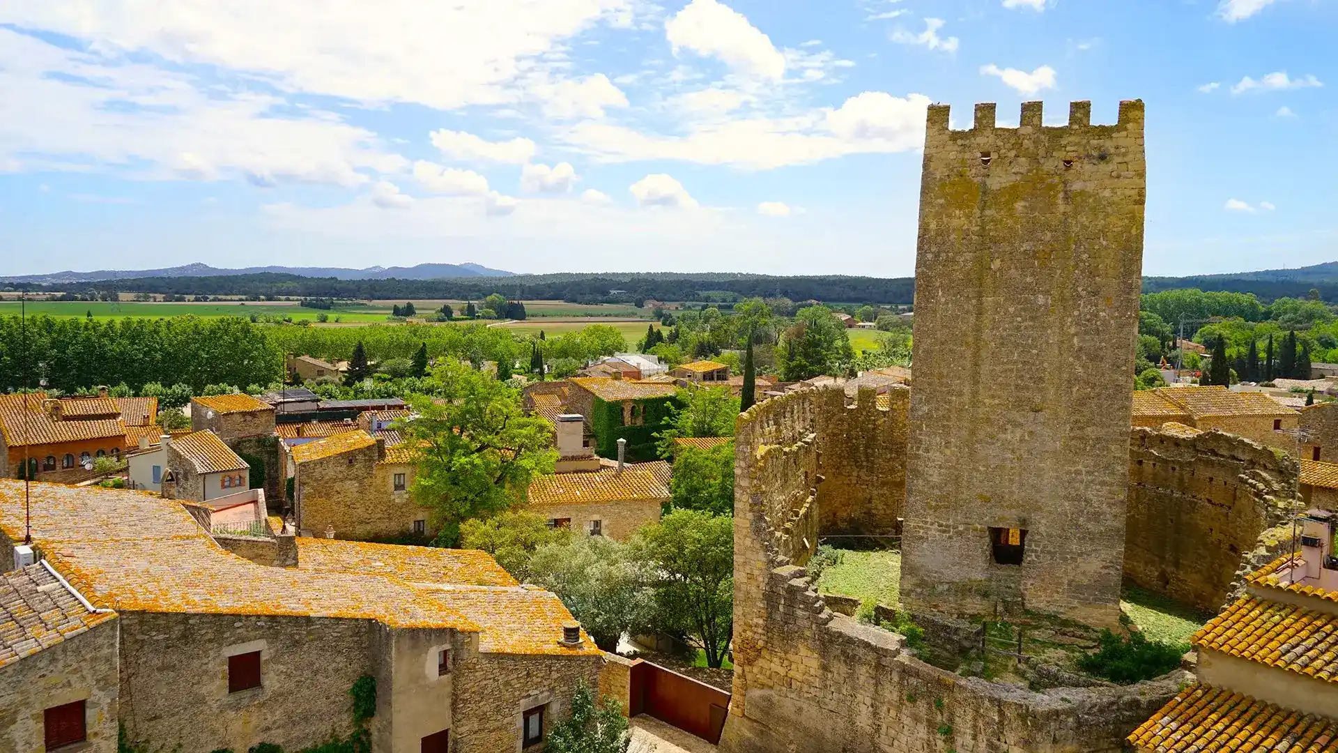 Vista de un pueblo con torre de piedra y paisaje verde al fondo.