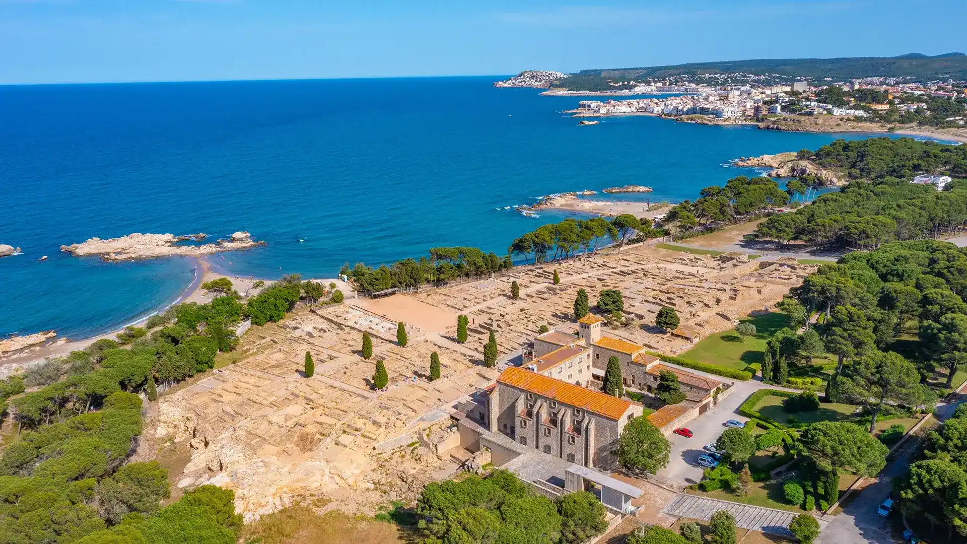 Vista a&eacute;rea de ruinas antiguas junto al mar y un pueblo en la distancia.