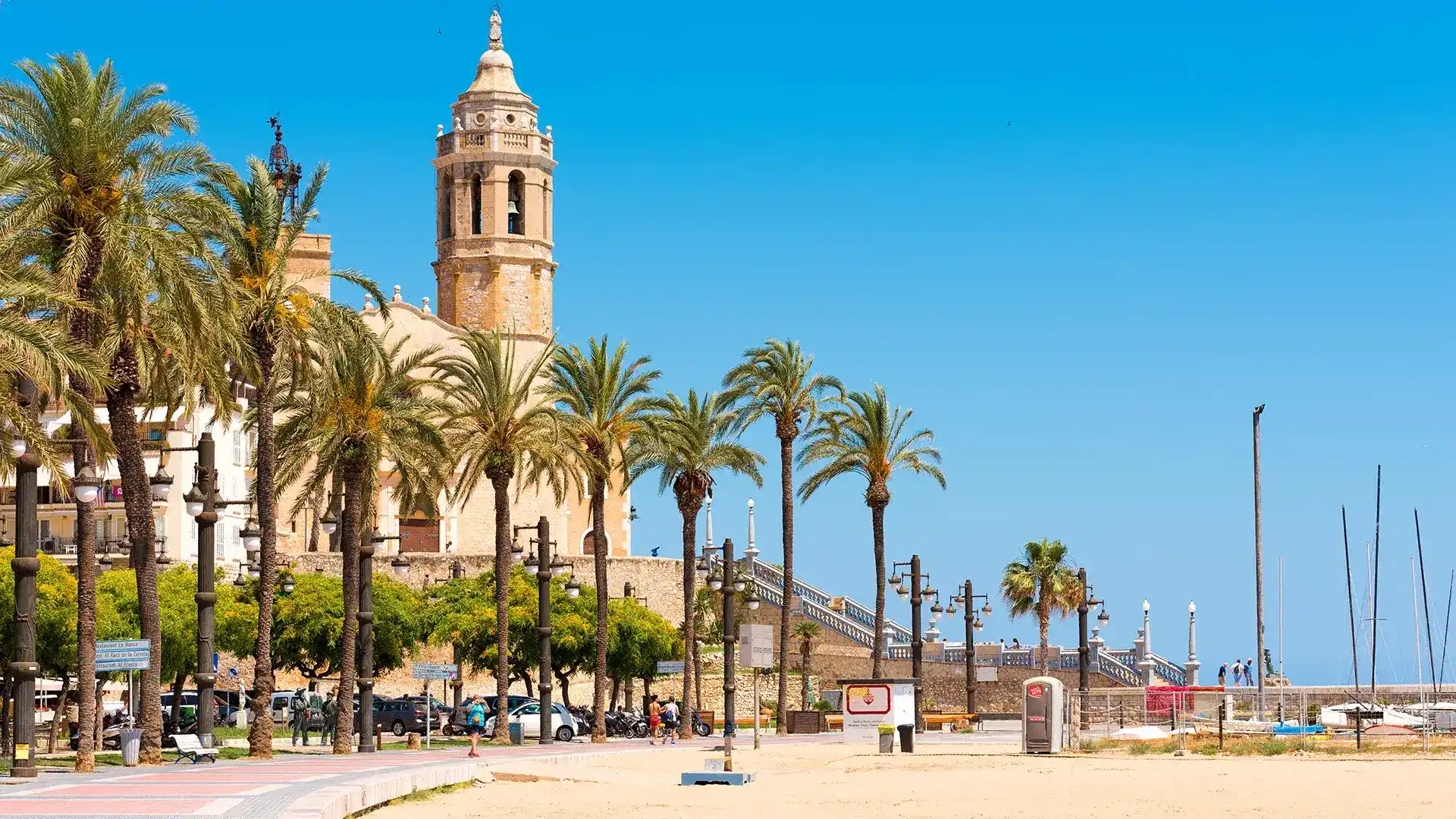 Playa con palmeras y una iglesia al fondo bajo un cielo azul.