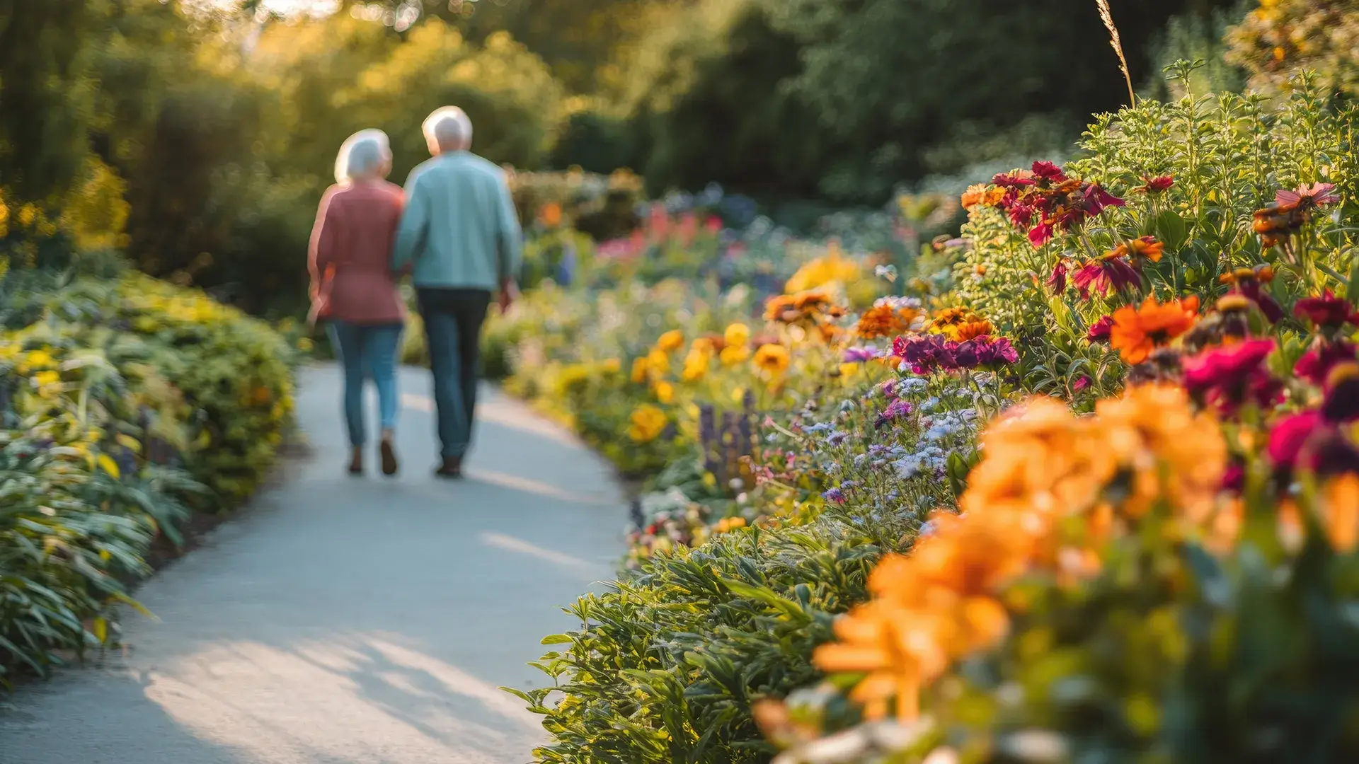 Pareja mayor caminando por un jard&iacute;n lleno de flores bajo el sol.