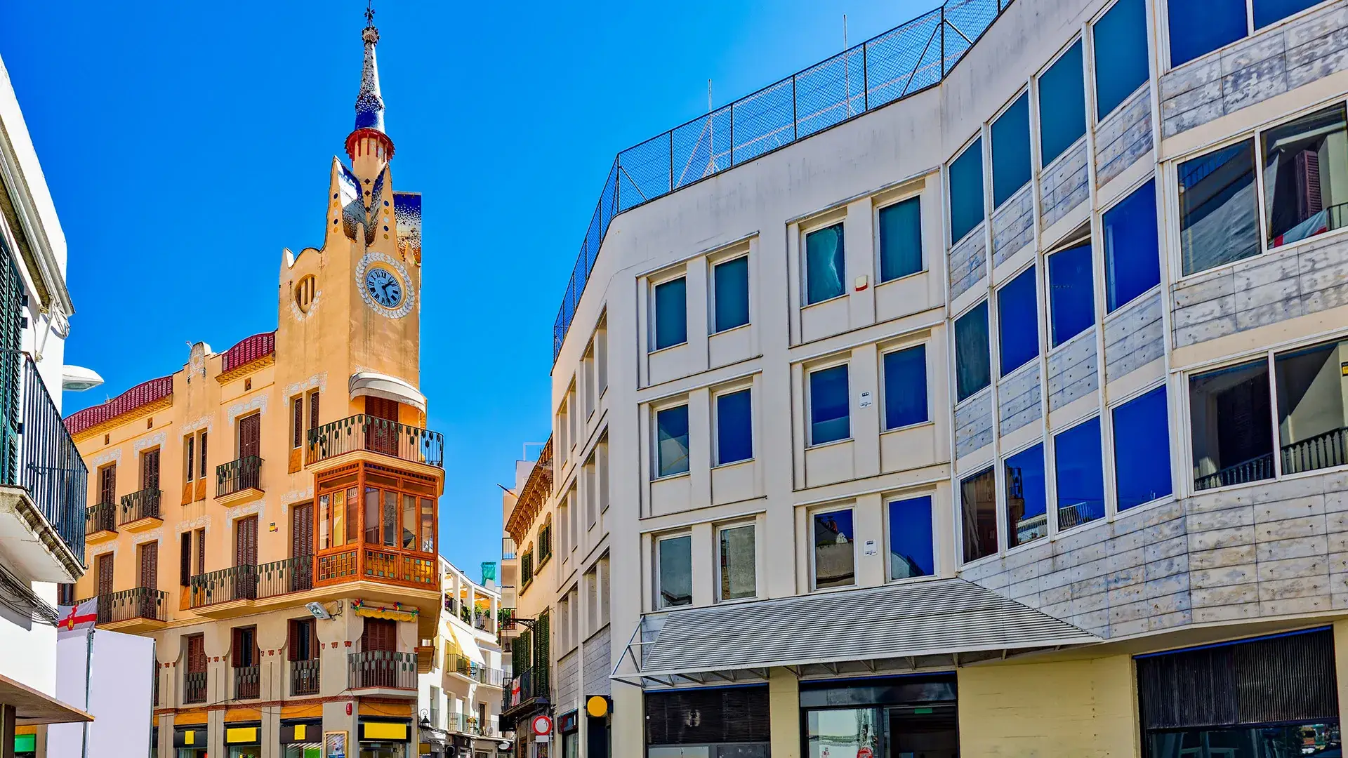 Torre con reloj en edificio de esquina junto a un moderno edificio blanco.