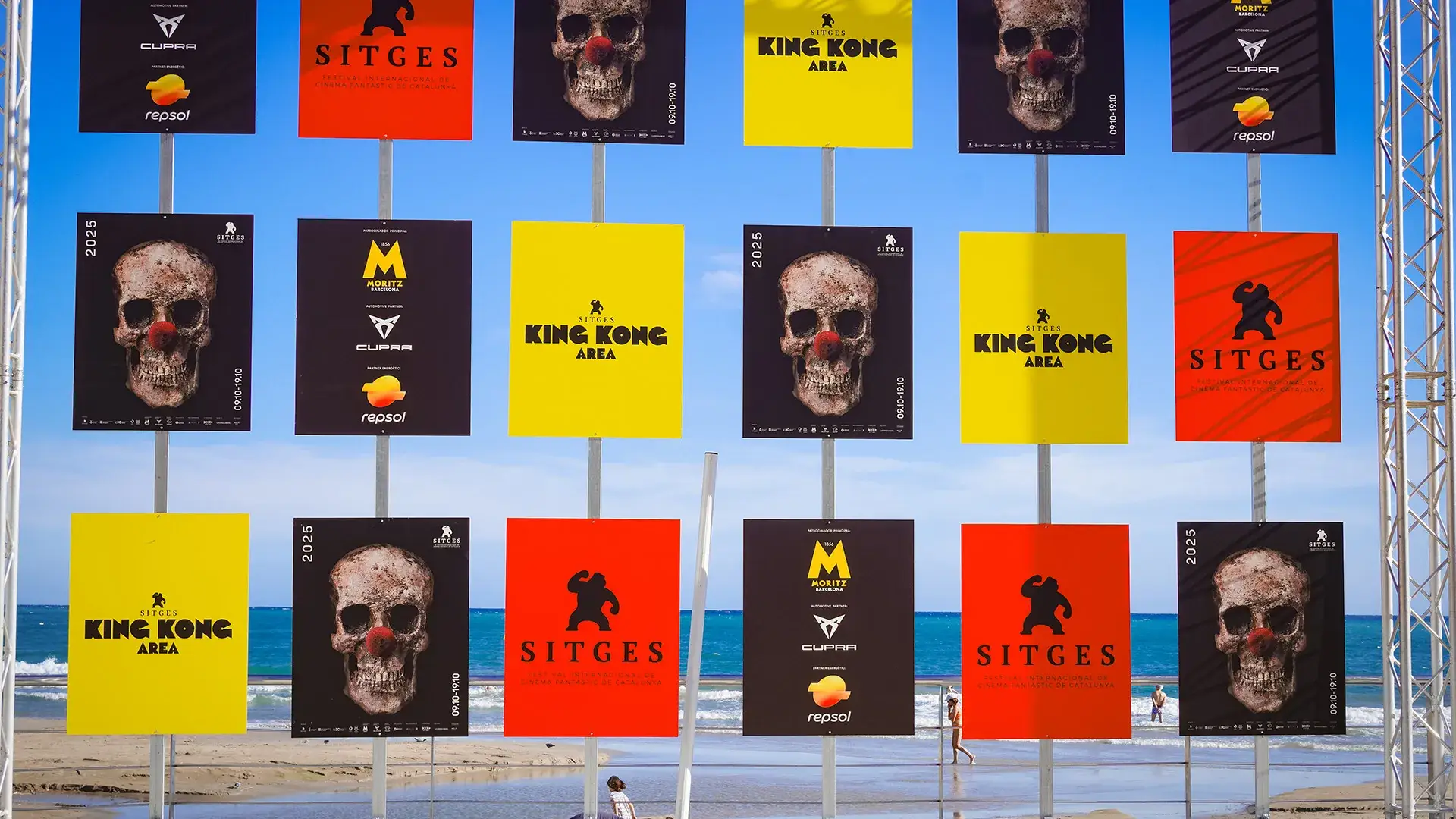 Carteles del festival Sitges 2025 con calaveras y colores vibrantes en la playa.