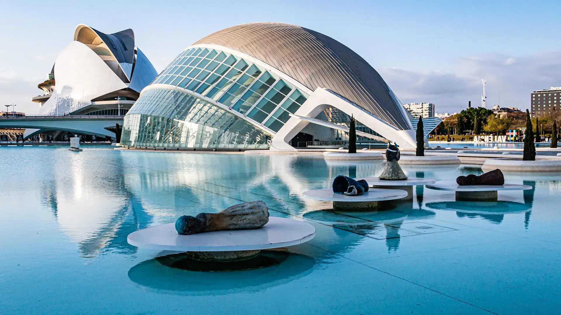 Edificios futuristas reflejados en un estanque bajo un cielo despejado.
