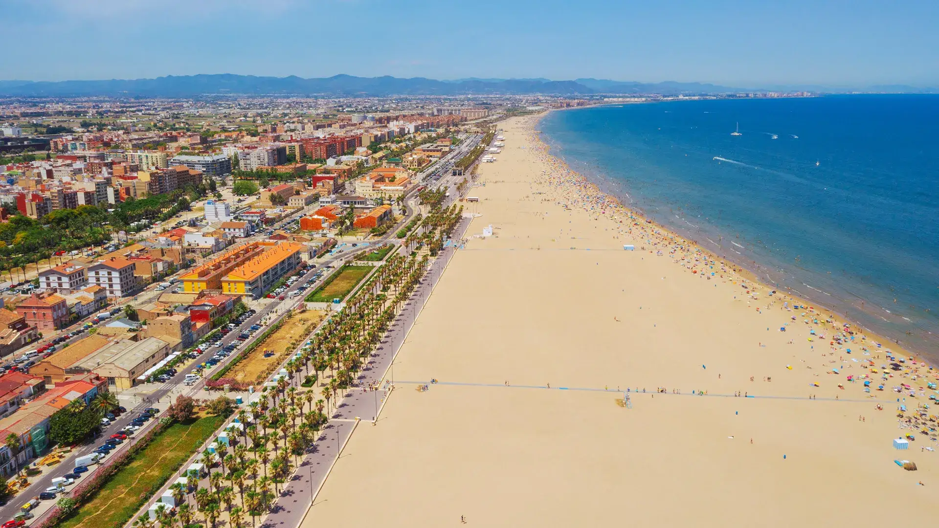 Vista a&eacute;rea de una playa concurrida junto a la ciudad, con mar azul.