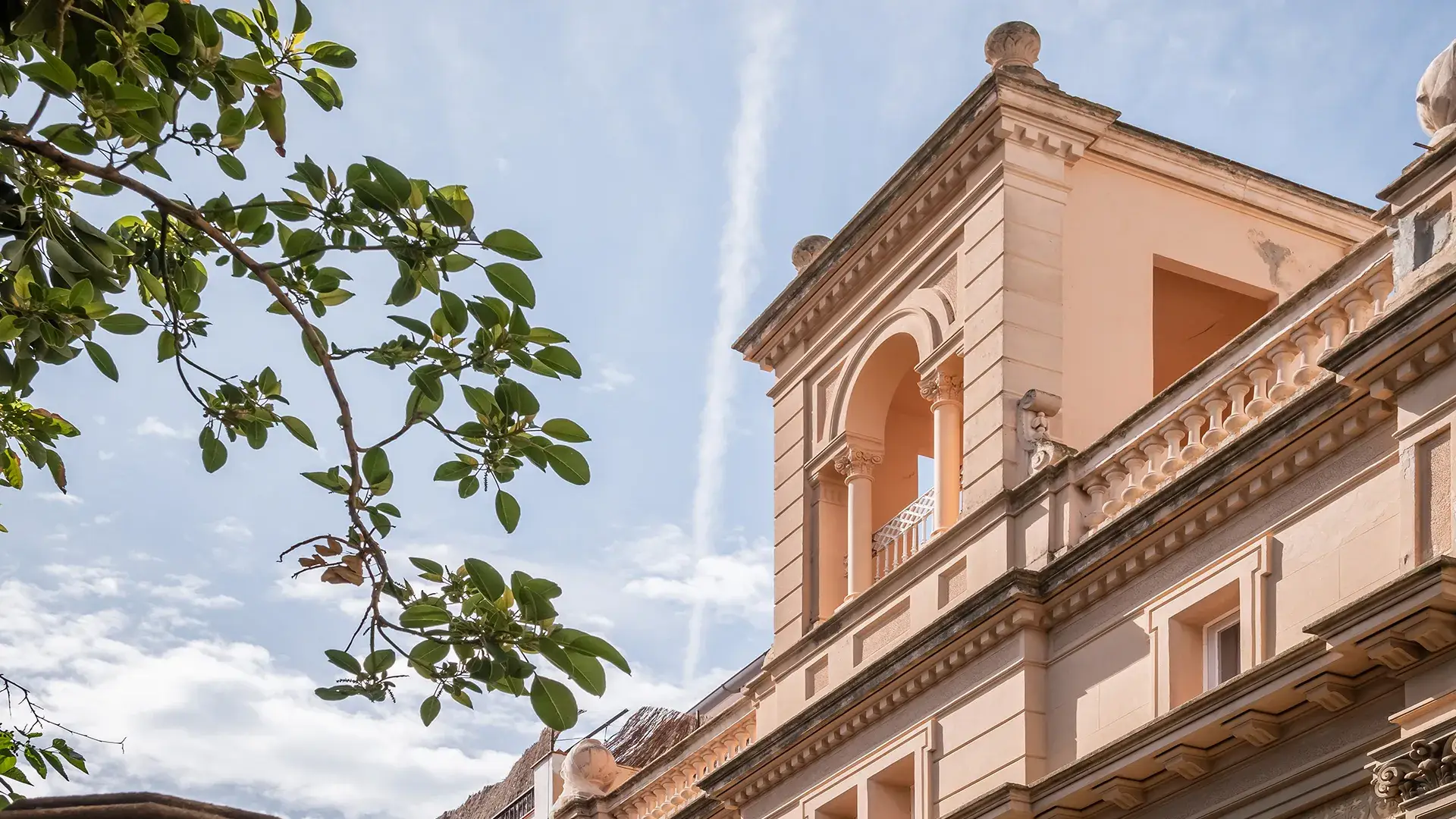 Edificio hist&oacute;rico con detalles arquitect&oacute;nicos y ramas verdes al frente.