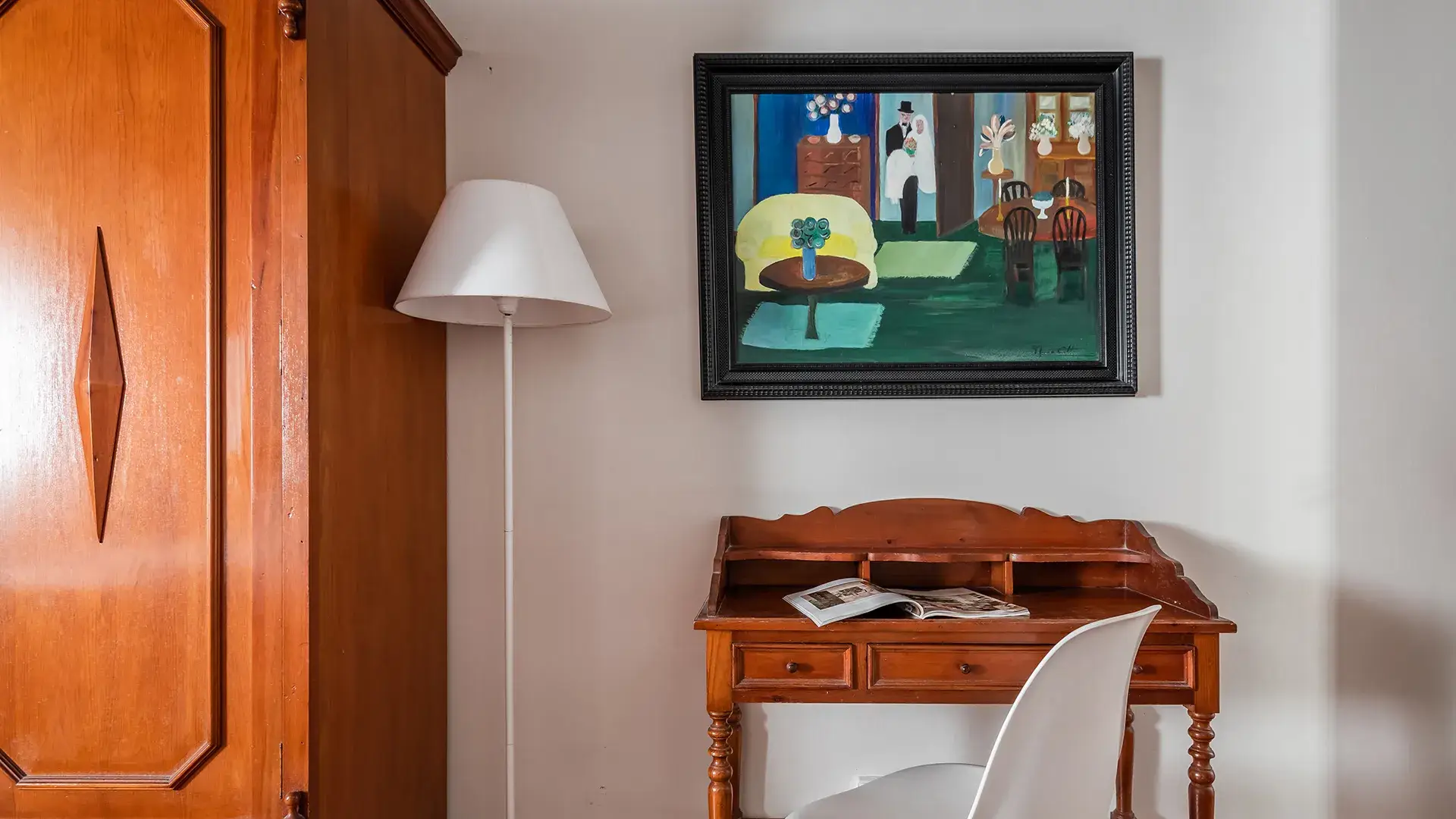 Habitaci&oacute;n con escritorio de madera, silla blanca y cuadro colorido en la pared.