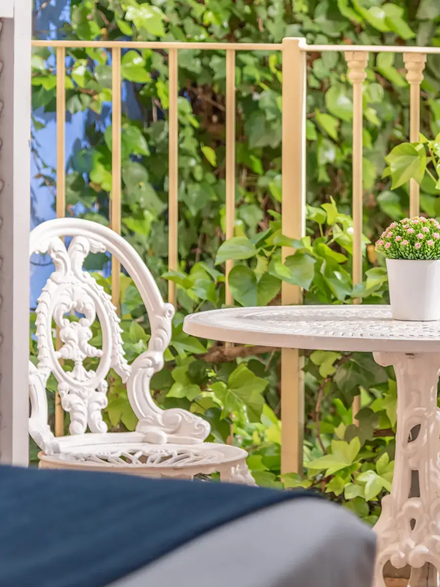 Silla y mesa blancas en un patio con plantas y cerca de madera.