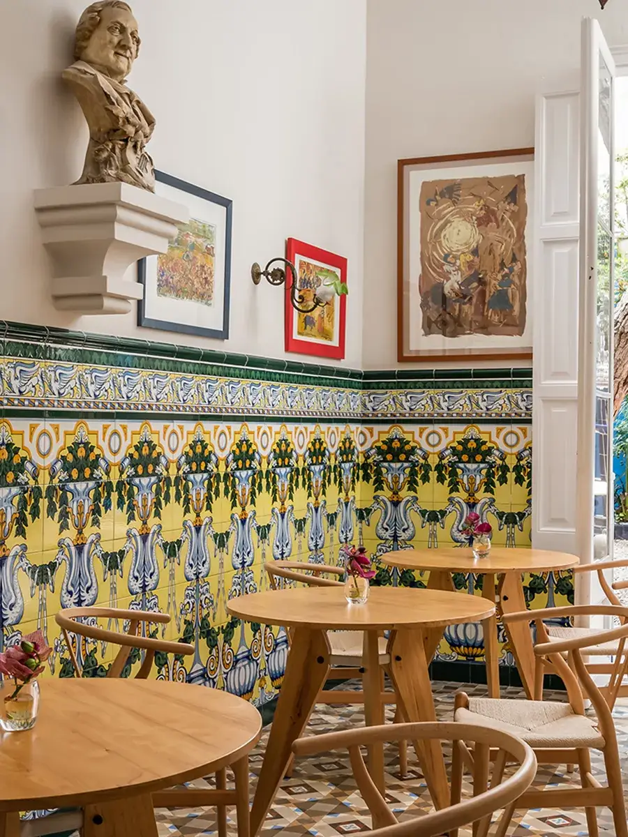 Sala con mesas de madera, azulejos coloridos y un busto sobre el muro.