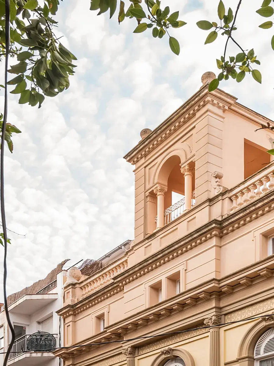 Edificio antiguo con columnas, rodeado de hojas verdes bajo un cielo nublado.