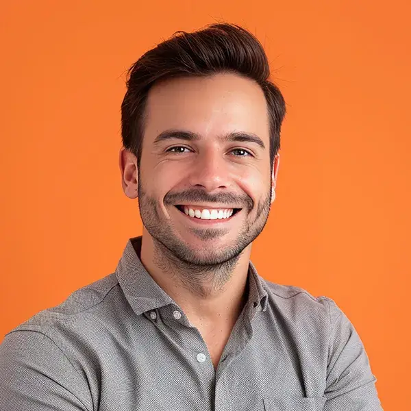 Hombre sonriente con camisa gris sobre fondo naranja.