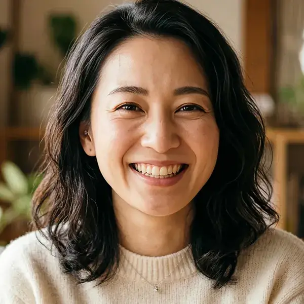 Mujer sonriendo, de cabello oscuro, usando un su&eacute;ter claro.