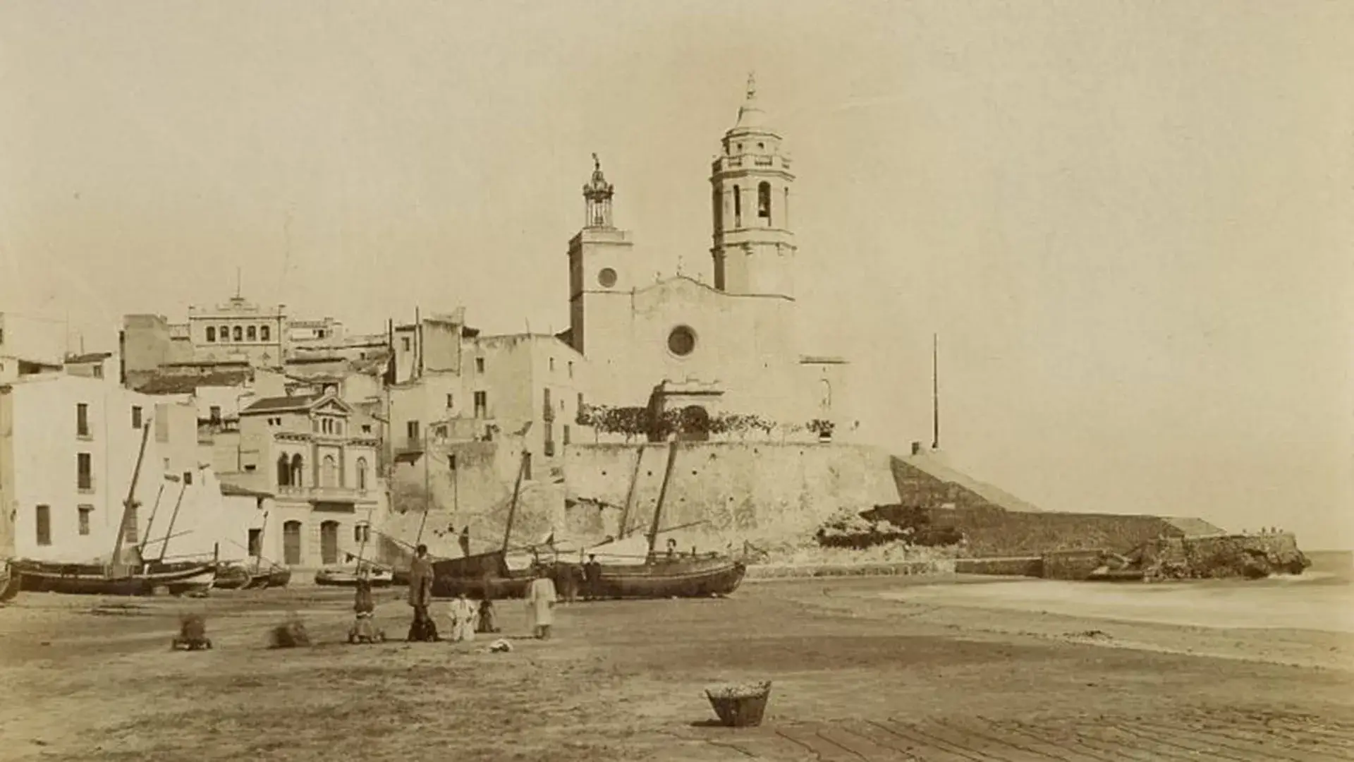 Iglesia antigua junto al mar con casas y barcas alrededor, en una foto sepia.