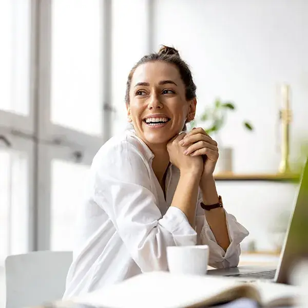 Una persona sonriendo frente a una computadora port&aacute;til en una oficina iluminada.