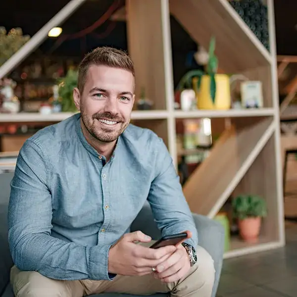 Hombre sonriendo sentado con un celular en un espacio moderno.