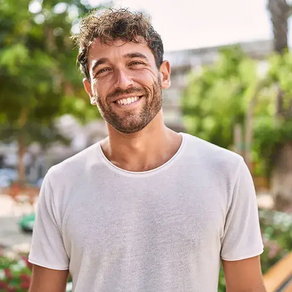 Hombre con barba y camiseta blanca sonriendo al aire libre.