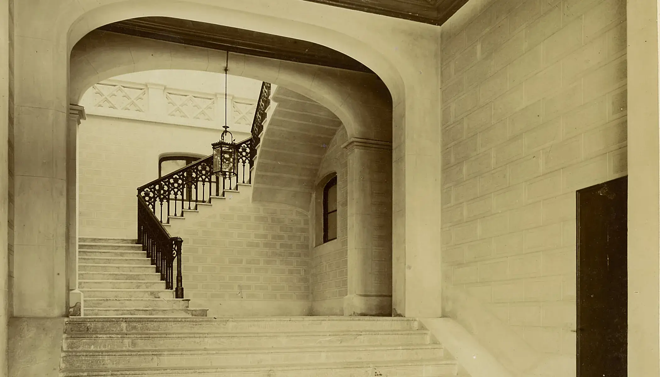 Escalera antigua con barandilla de metal y l&aacute;mpara colgante.