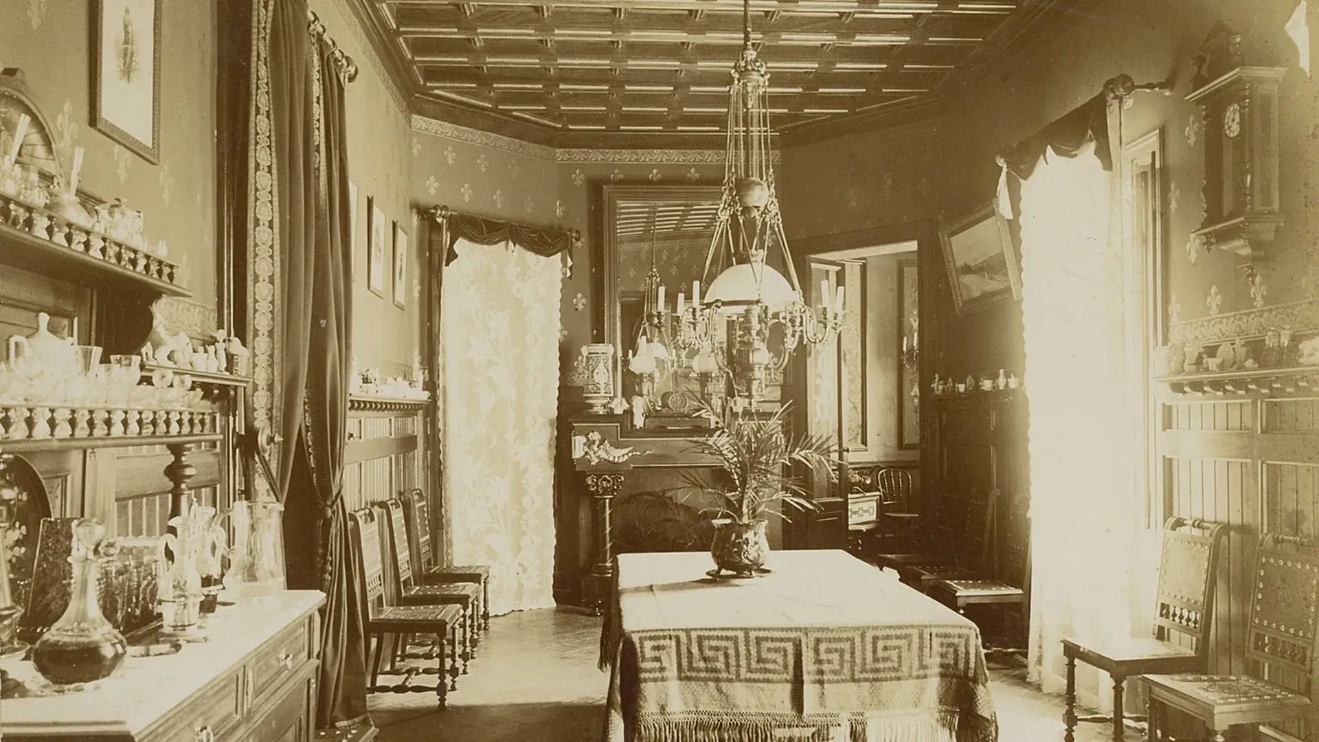 Sala antigua con mesa central, l&aacute;mpara de ara&ntilde;a y decoraciones detalladas.