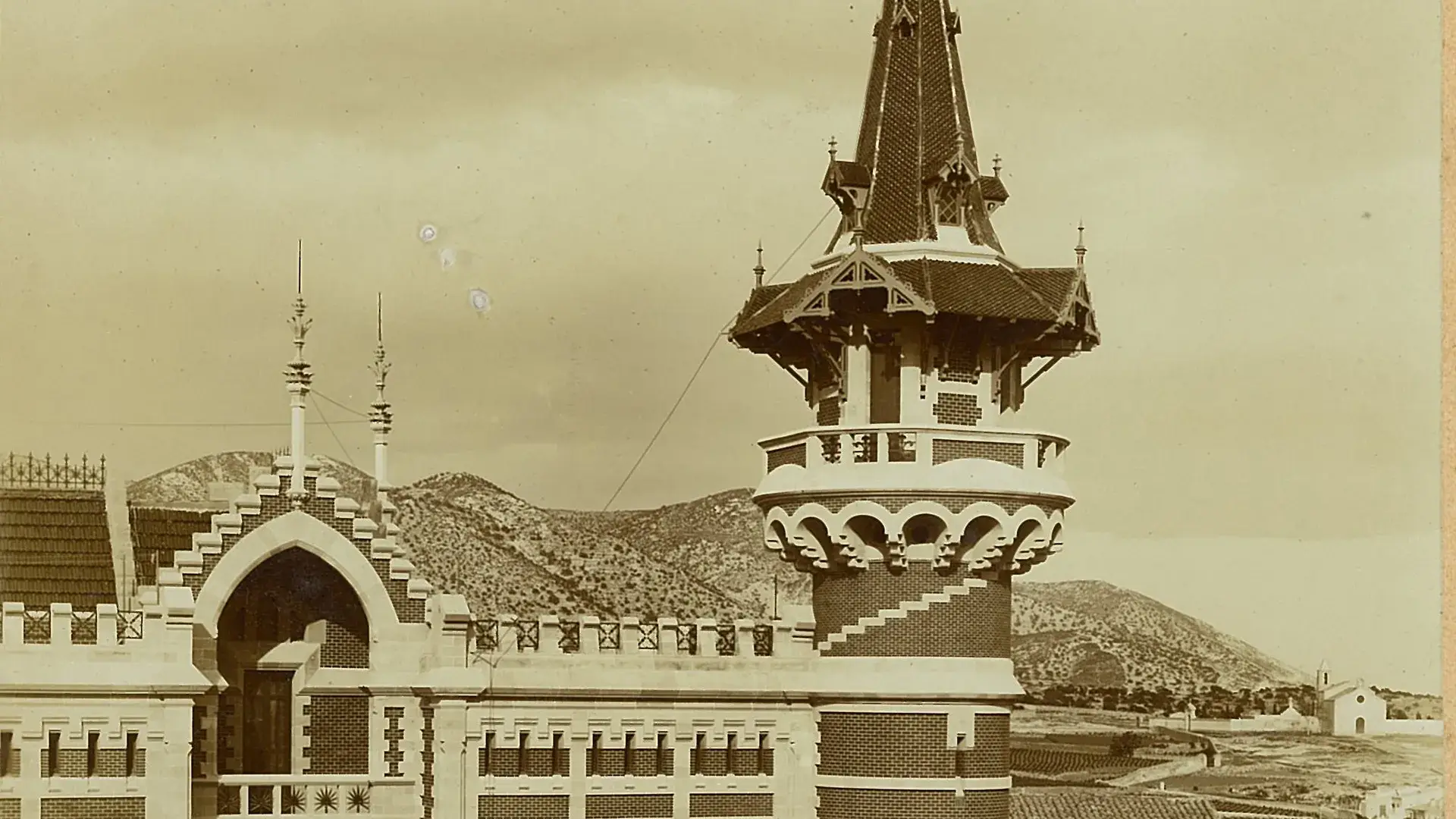 Torre con dise&ntilde;o arquitect&oacute;nico antiguo y monta&ntilde;as al fondo.