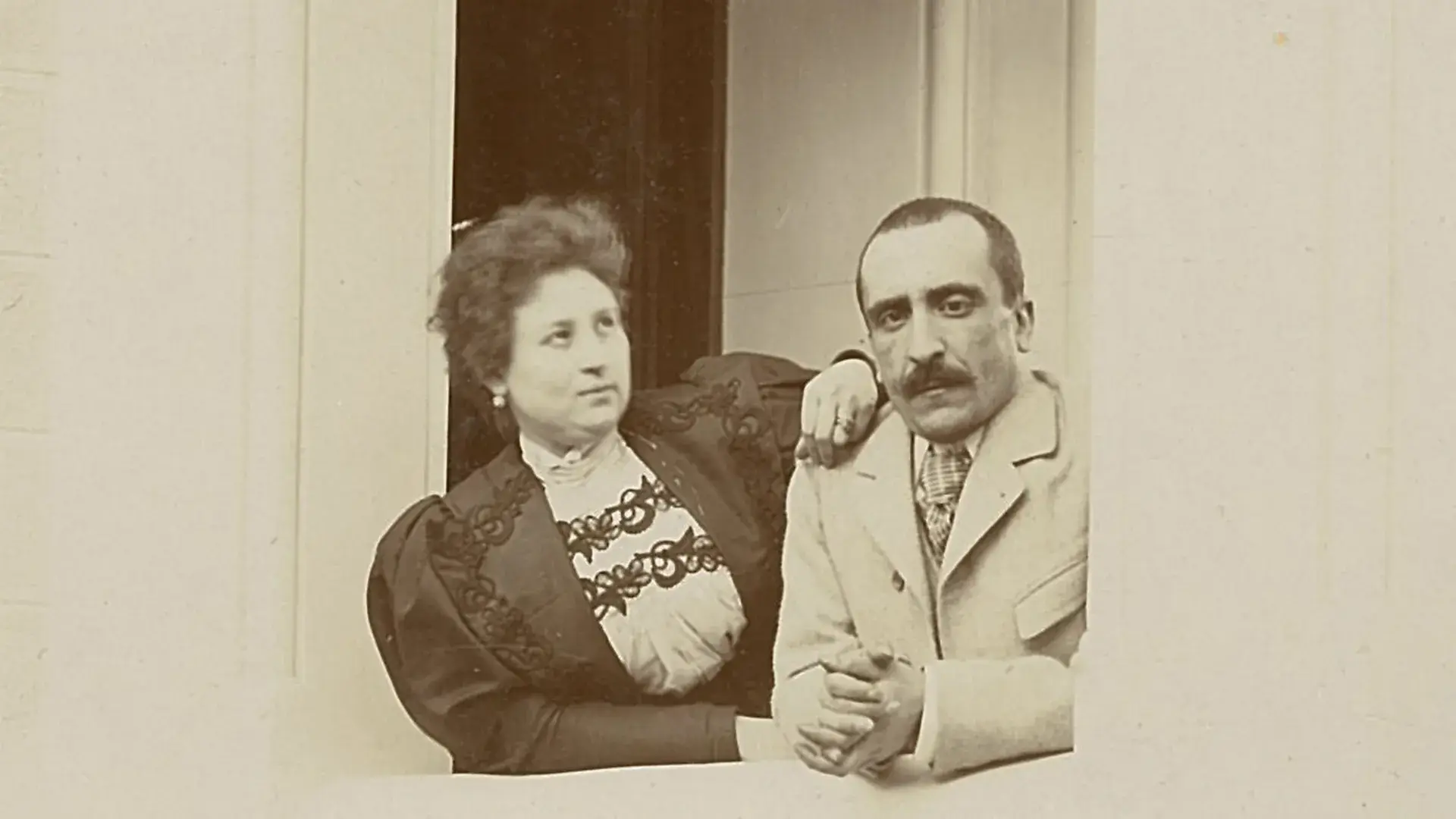 Una pareja posando en un balc&oacute;n, con atuendos formales de &eacute;poca.