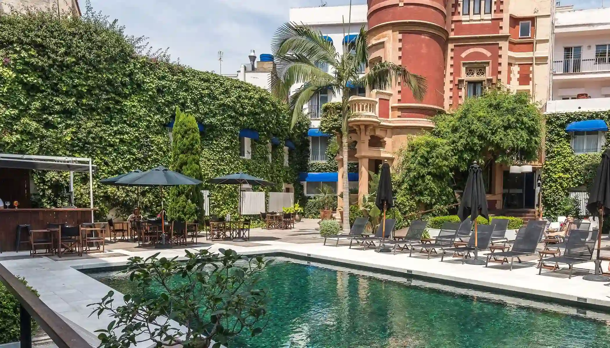 Piscina al aire libre rodeada de vegetaci&oacute;n y un edificio hist&oacute;rico.
