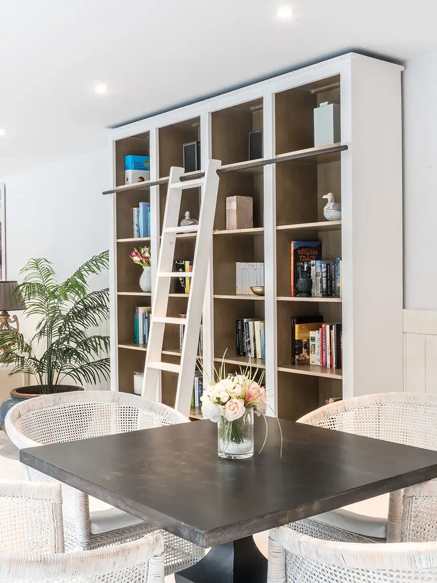 Estanter&iacute;a con escalera en sala moderna, mesa y sillas de mimbre.