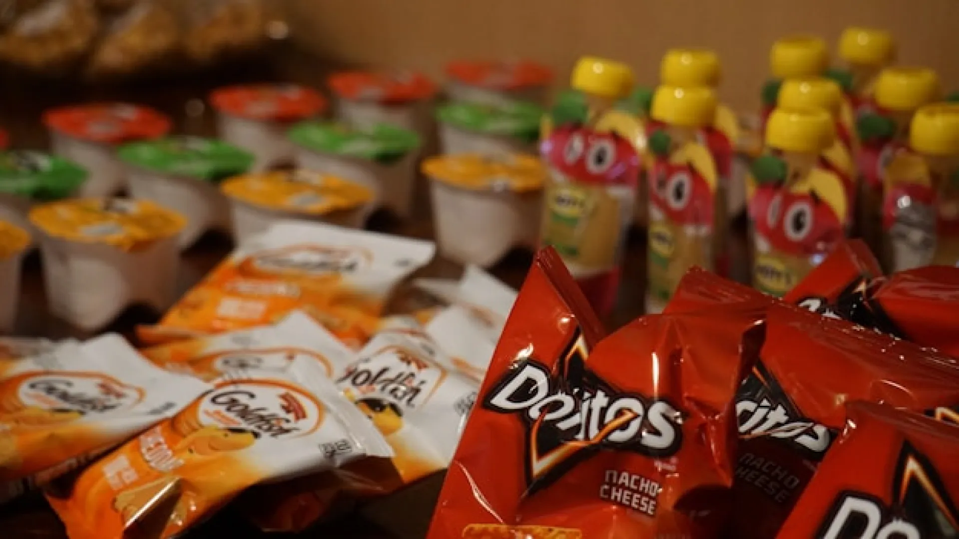 Desorden de snacks y botellas en estanter&iacute;a, con empaques de queso Doritos