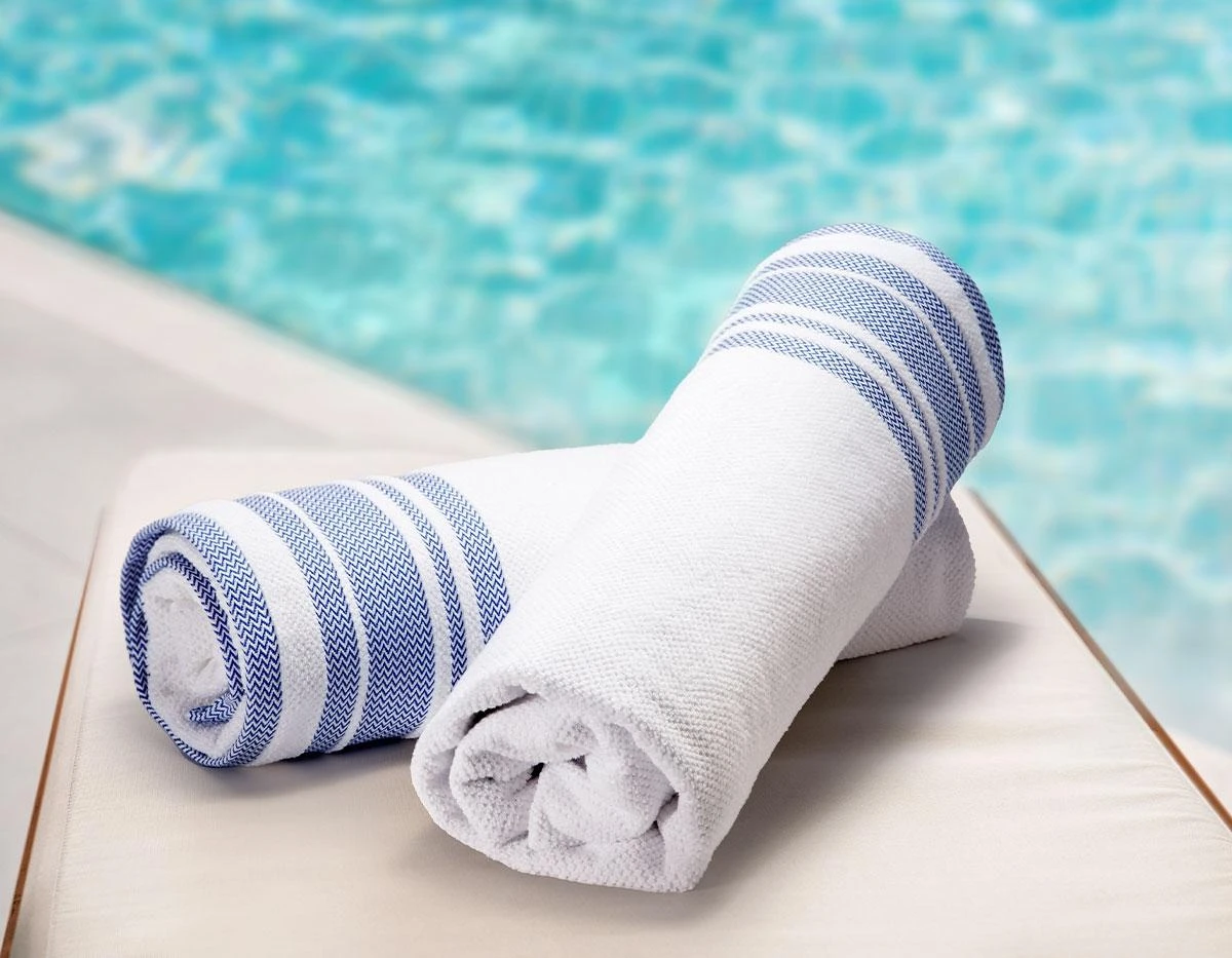 Toallas blancas y azules enrolladas junto a piscina, desenfocada al fondo