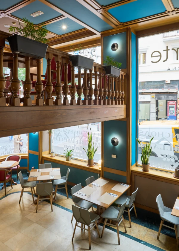 Restaurante moderno con ventanas grandes, plantas y mesas ordenadas.