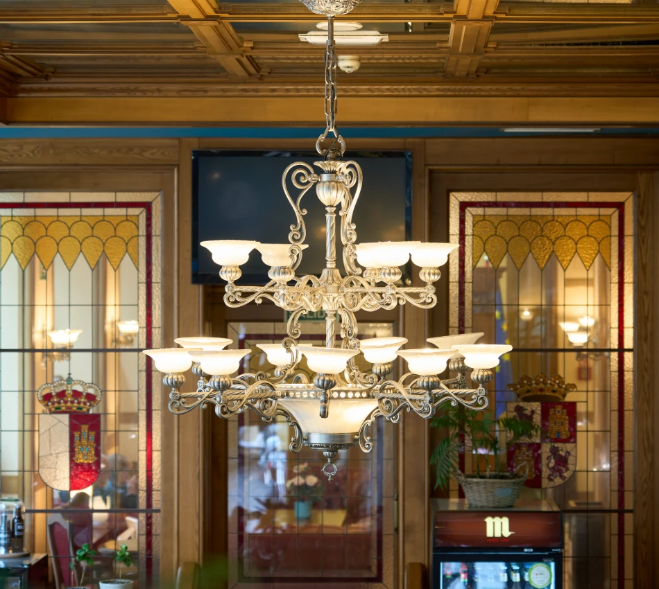 L&aacute;mpara de ara&ntilde;a elegante en un interior con vitrales y detalles decorativos.