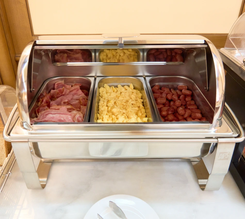 Buffet con tocino, huevos revueltos y salchichas en bandejas de acero inoxidable.