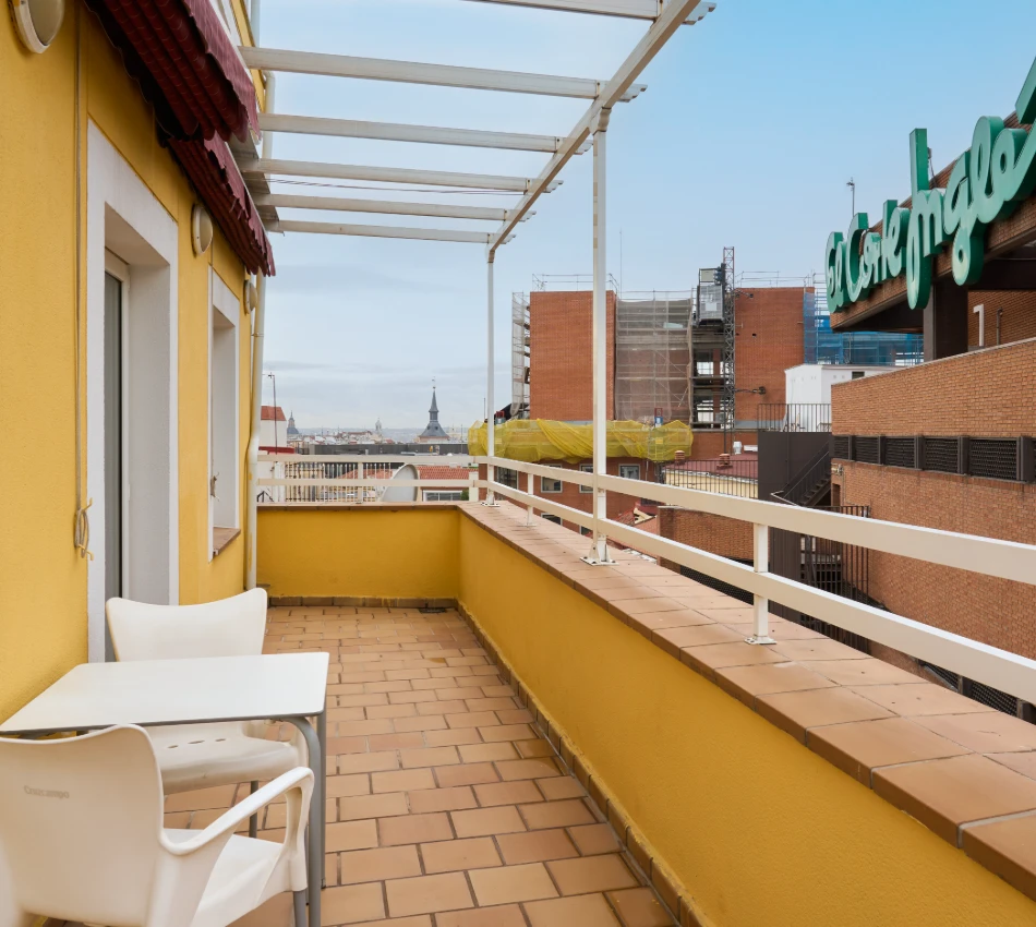 Terraza con mesa, sillas y vista de la ciudad, edificios de ladrillo a la derecha.