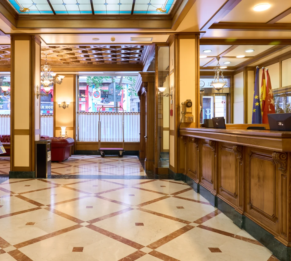 Recepci&oacute;n de hotel elegante con mostrador de madera y luces decorativas.