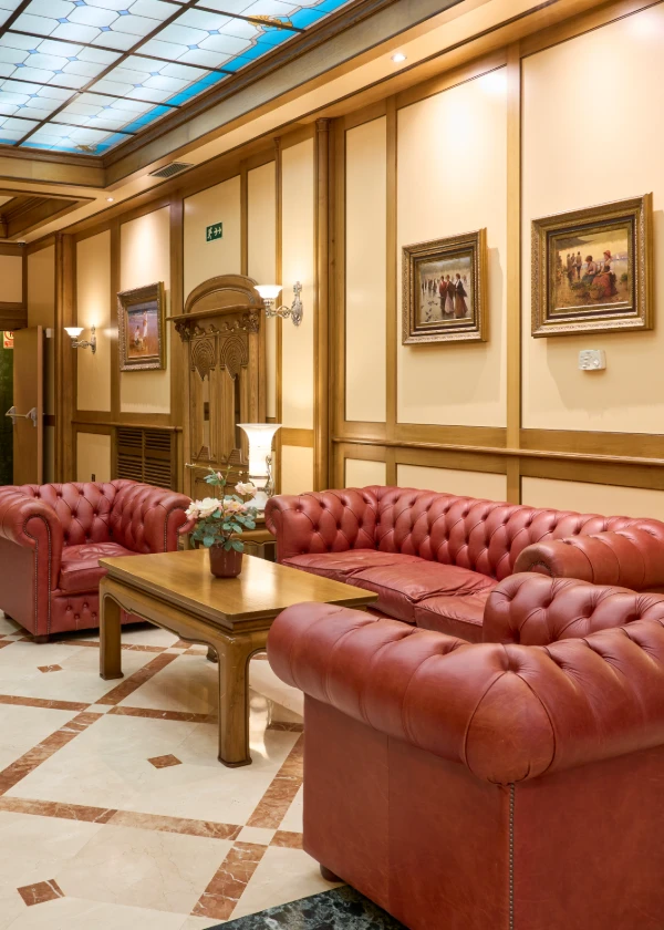 Sala elegante con sillones de cuero rojo, mesa de madera y cuadros en la pared.