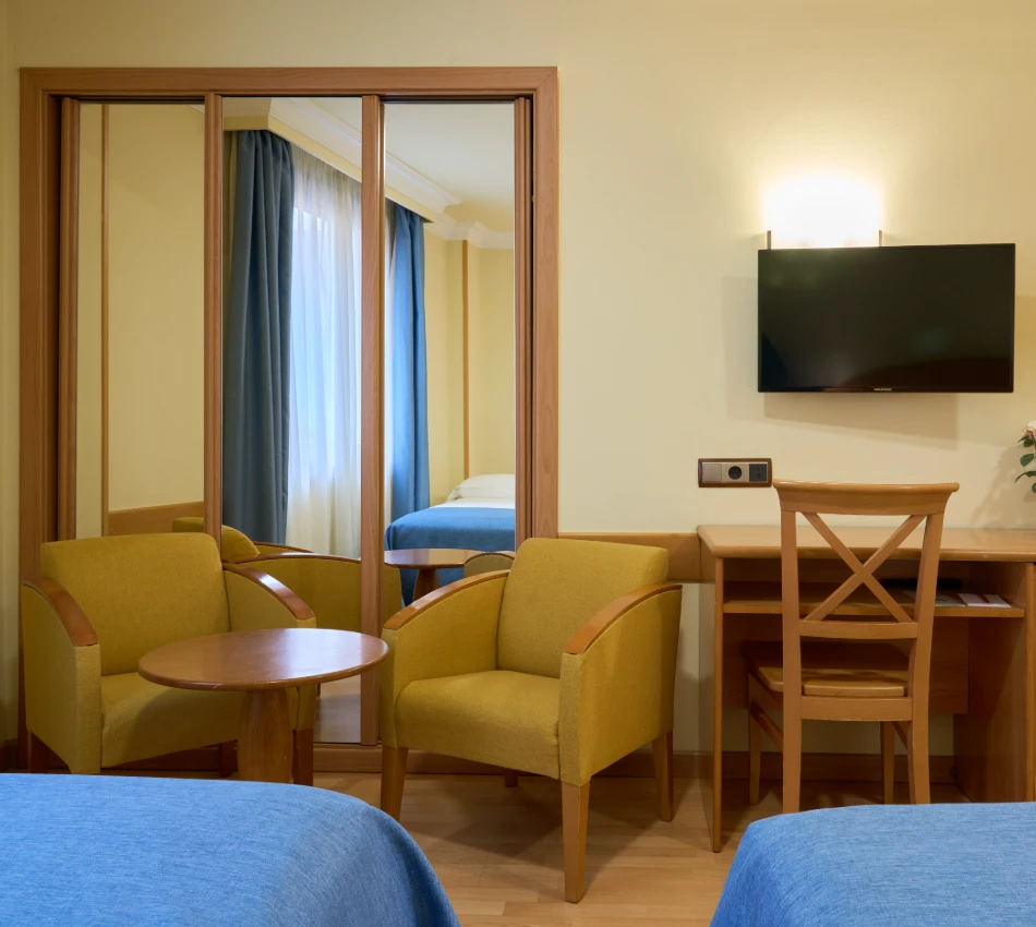 Habitaci&oacute;n con sillones amarillos, mesa, televisor y gran espejo.