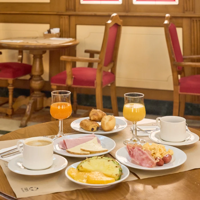 Desayuno variado con jugos, caf&eacute;, fruta, embutidos y pan en mesa de restaurante.