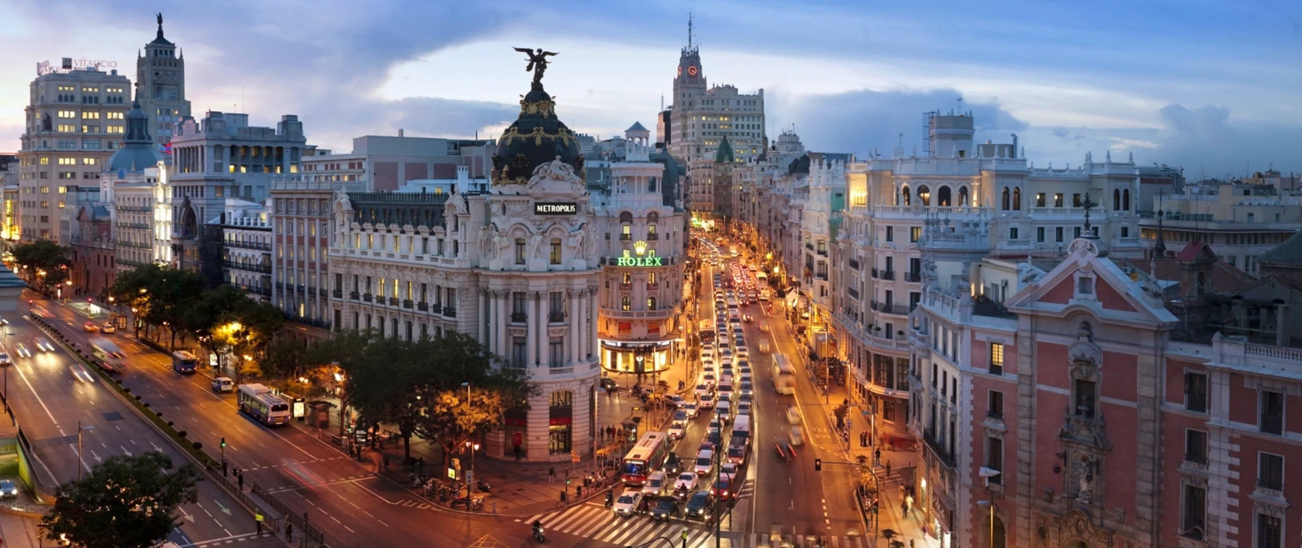 Vista nocturna de una calle con edificios iluminados y tr&aacute;fico en movimiento.