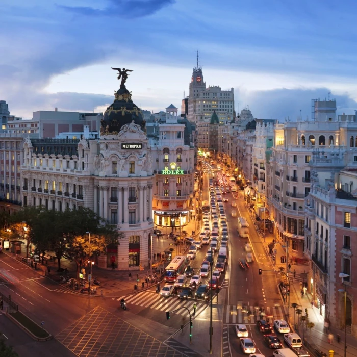 Vista nocturna de la Gran V&iacute;a de Madrid con tr&aacute;fico y edificios iluminados.