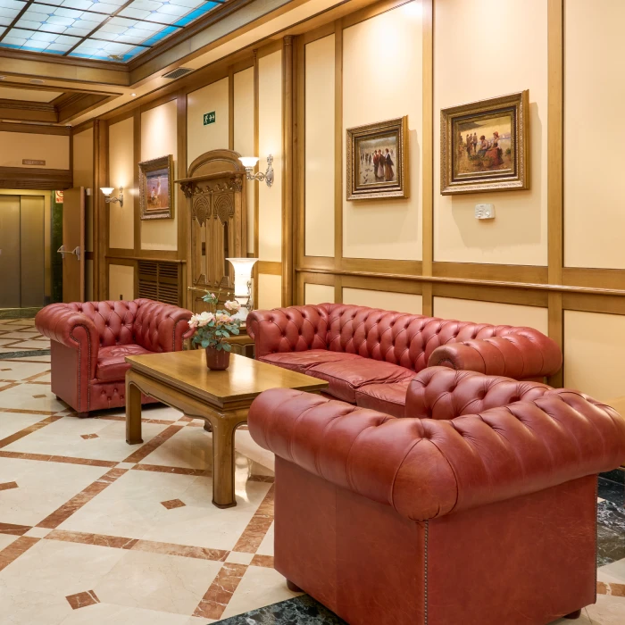 Sala elegante con sof&aacute;s de cuero rojo y mesa de madera. Cuadros en la pared.