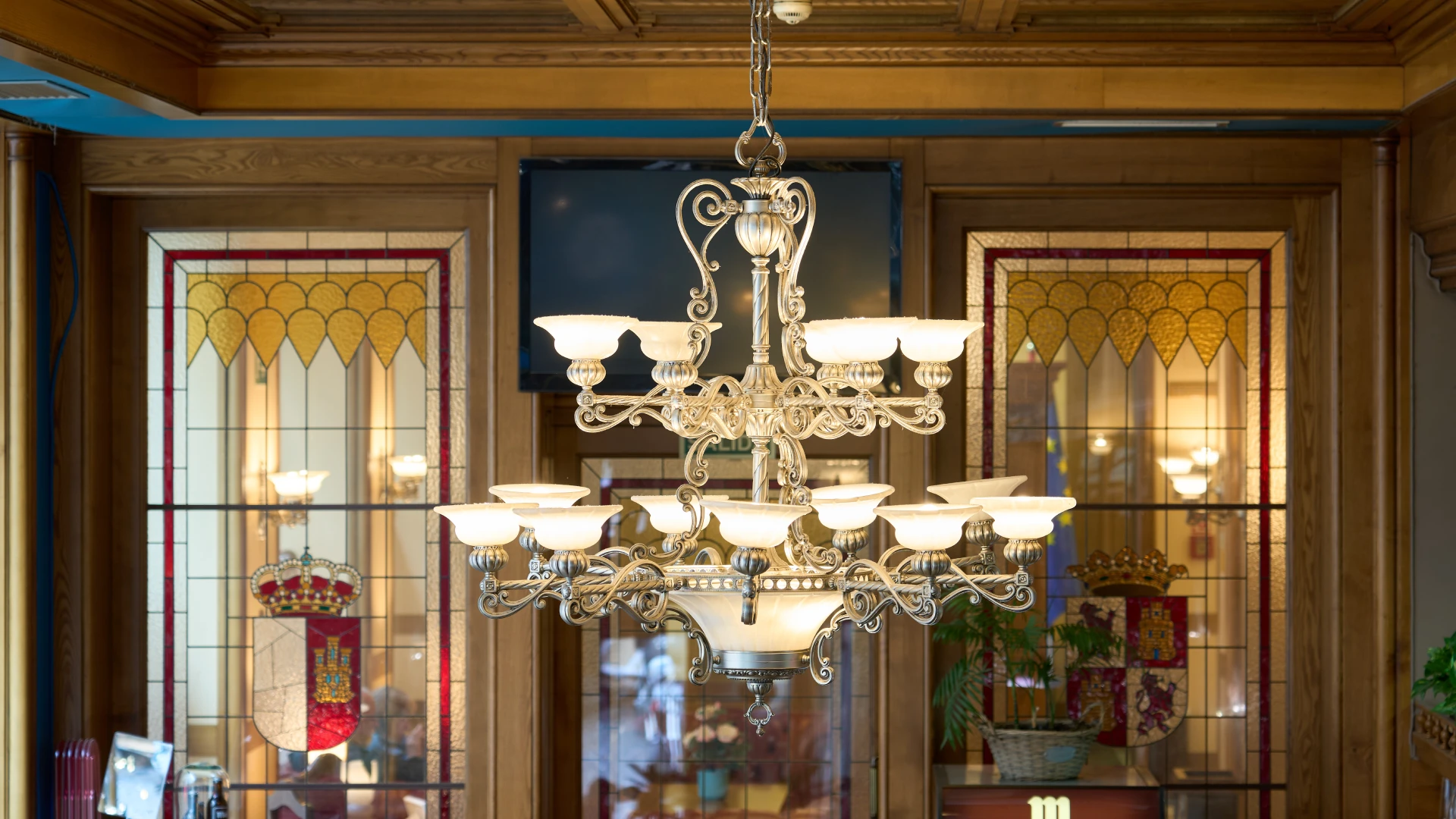 L&aacute;mpara de ara&ntilde;a elegante frente a vitrales decorativos en un interior cl&aacute;sico.