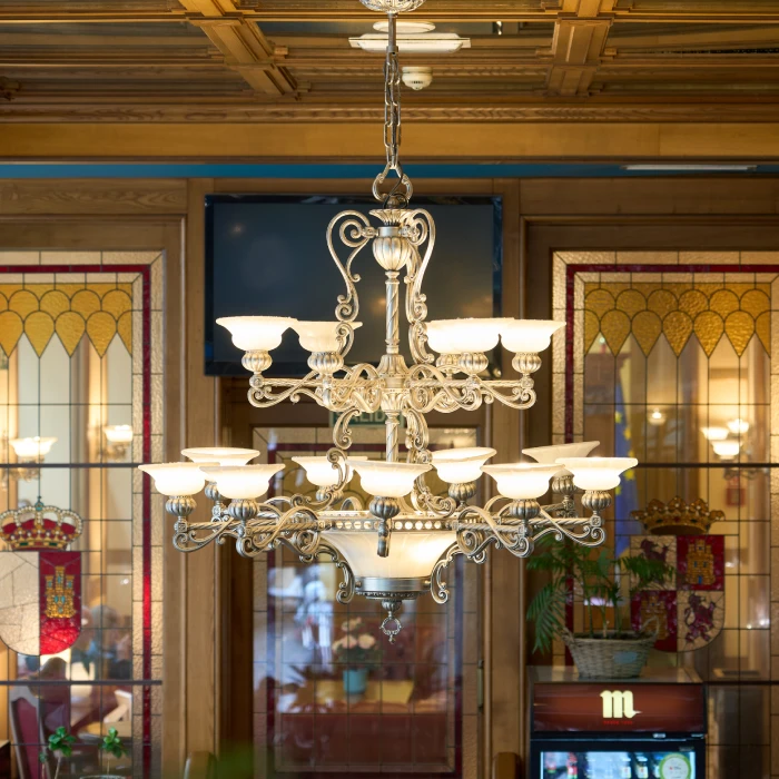 L&aacute;mpara de ara&ntilde;a cl&aacute;sica con fondo de vidrieras coloridas y emblemas.