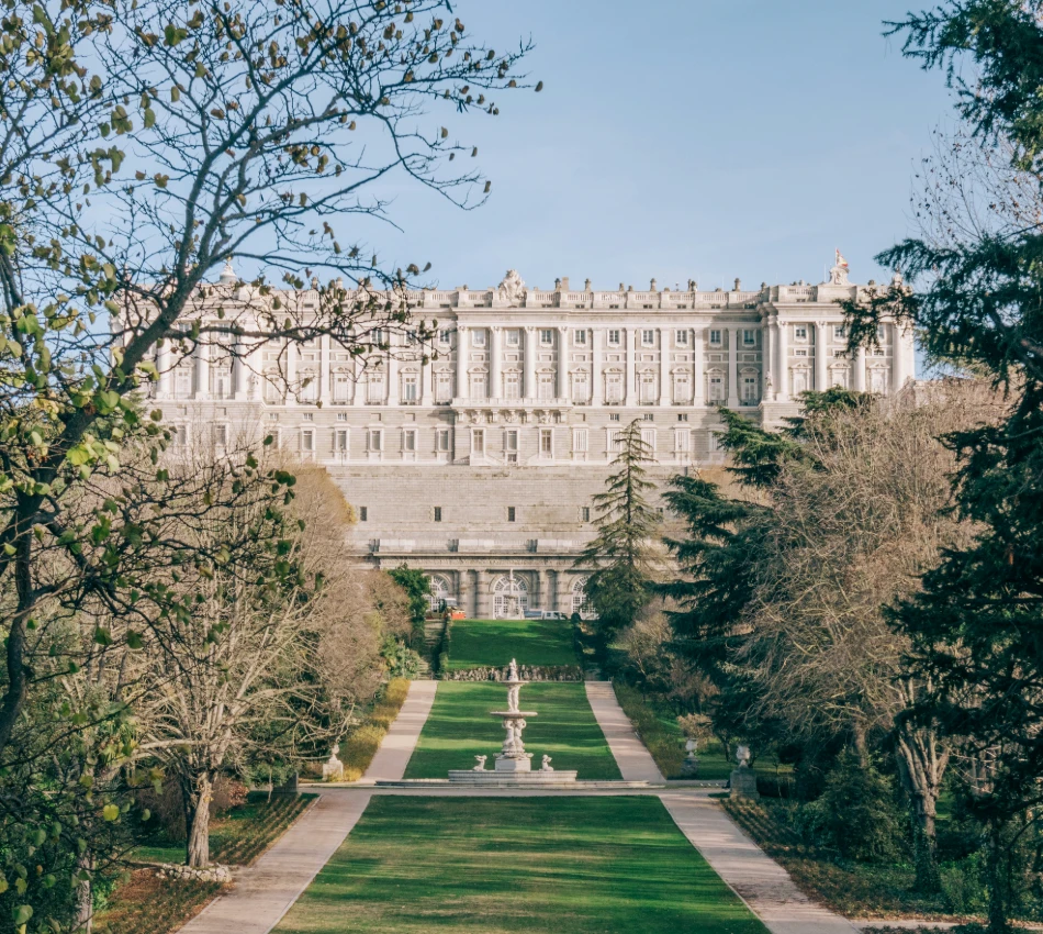 Palacio Real en Madrid rodeado de jardines y &aacute;rboles al atardecer.