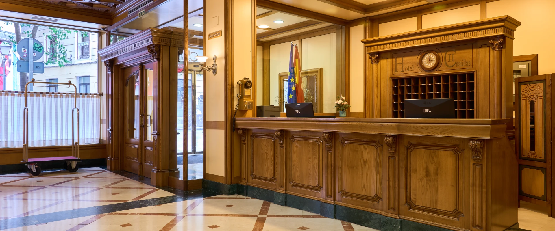 Recepci&oacute;n de hotel con mostrador de madera y carretilla para equipaje.