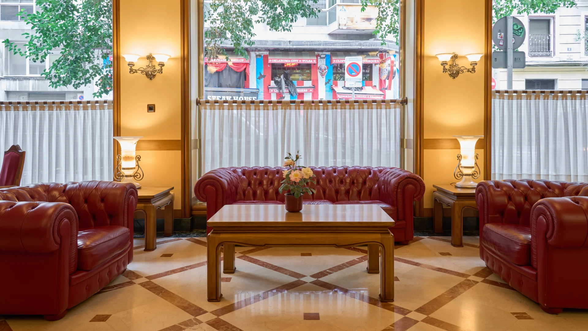 Sala con sillones de cuero rojo y mesas de madera, luz suave y ventana grande.